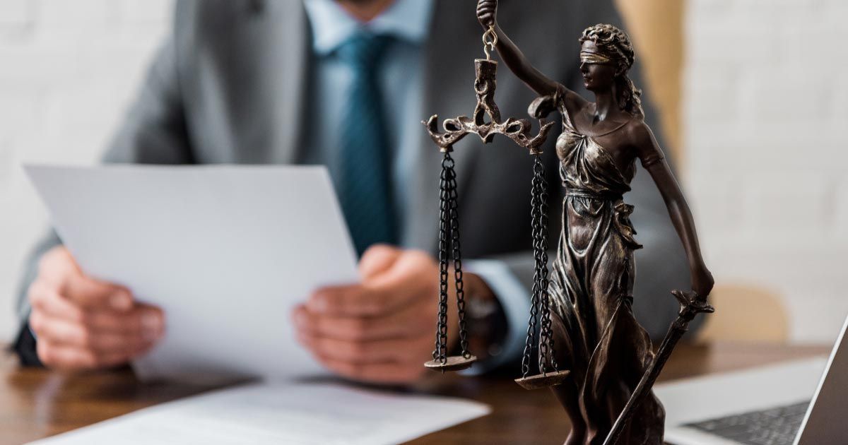 Bronze Lady Justice statue in front of a person reviewing documents at a desk