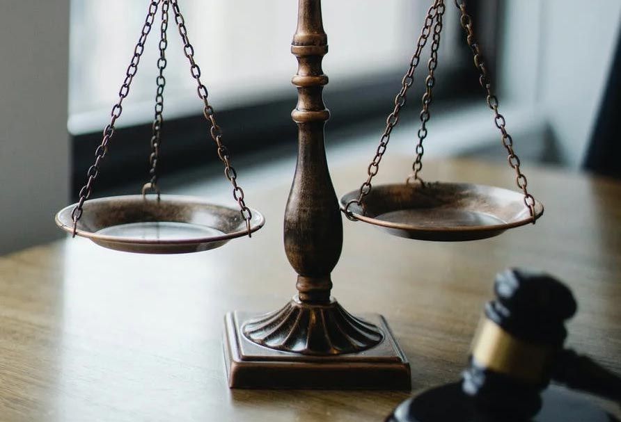 Bronze balance scale on a desk with a blurred gavel in the foreground