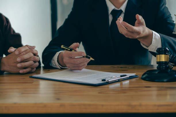 Two people in suits at a table, reviewing documents with a gavel nearby.