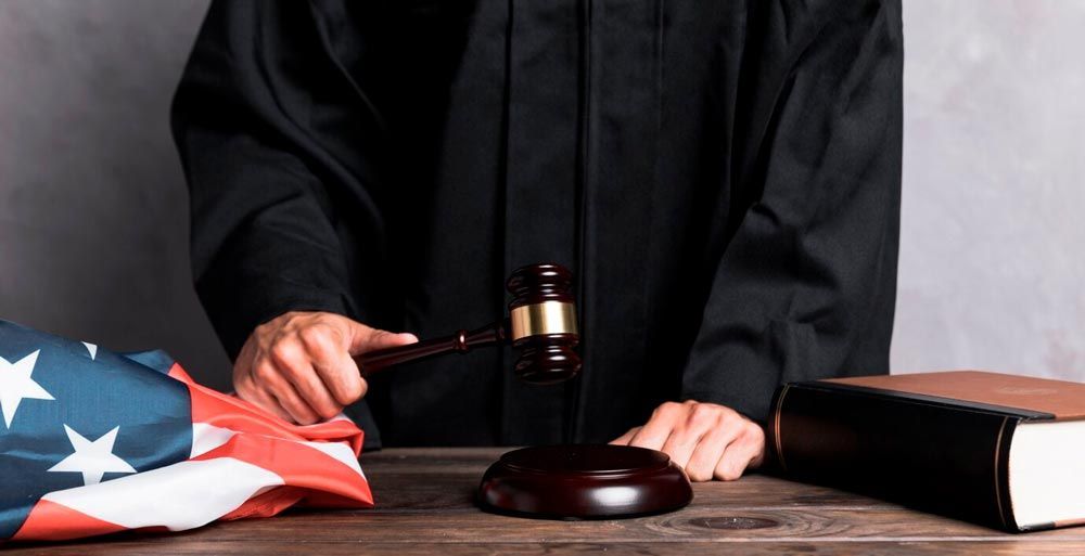 Judge’s hands with gavel over desk, folded U.S. flag and law books nearby
