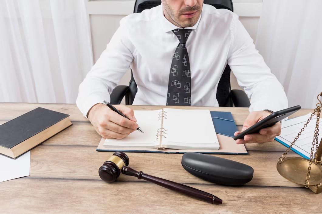 Lawyer in white shirt taking notes at desk with gavel, law books, and scales of justice