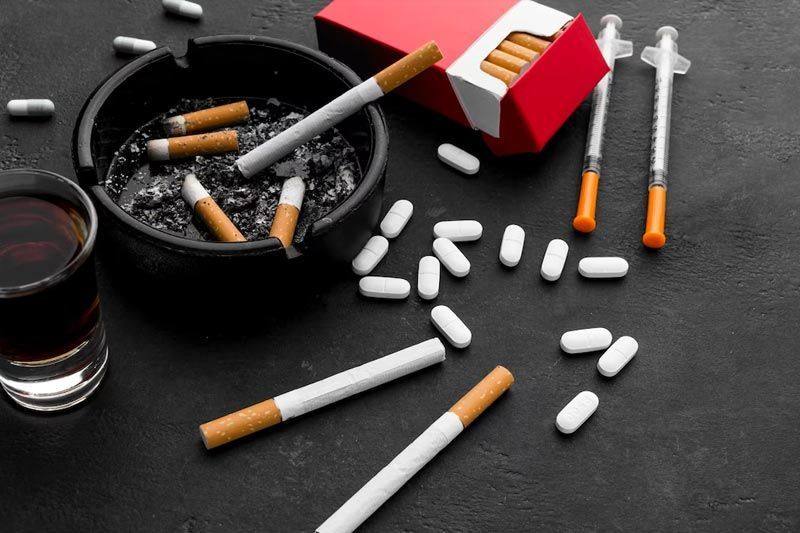 Cigarettes, ashtray, lighters, and spilled pills on a dark table with a glass of drink