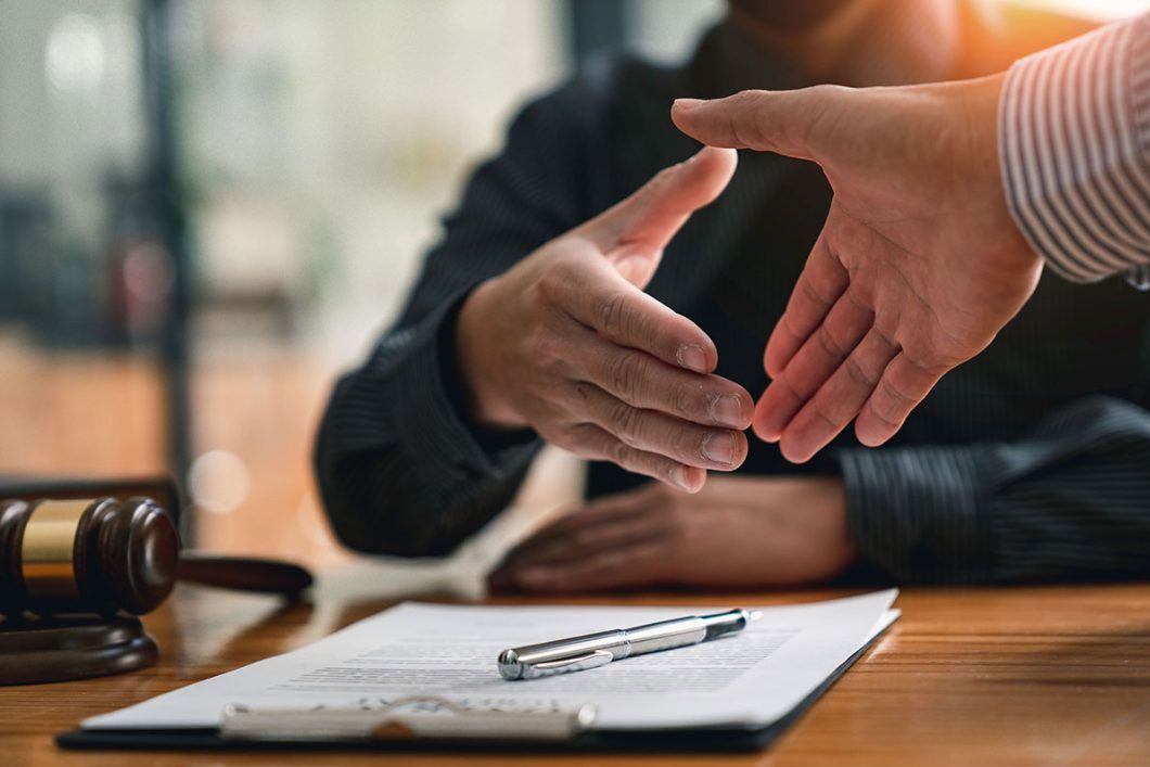 Hands shaking across a desk during a business meeting, with a pen and papers in the foreground