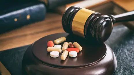 Judge’s gavel beside spilled pills on a wooden desk, suggesting legal or drug-related issues