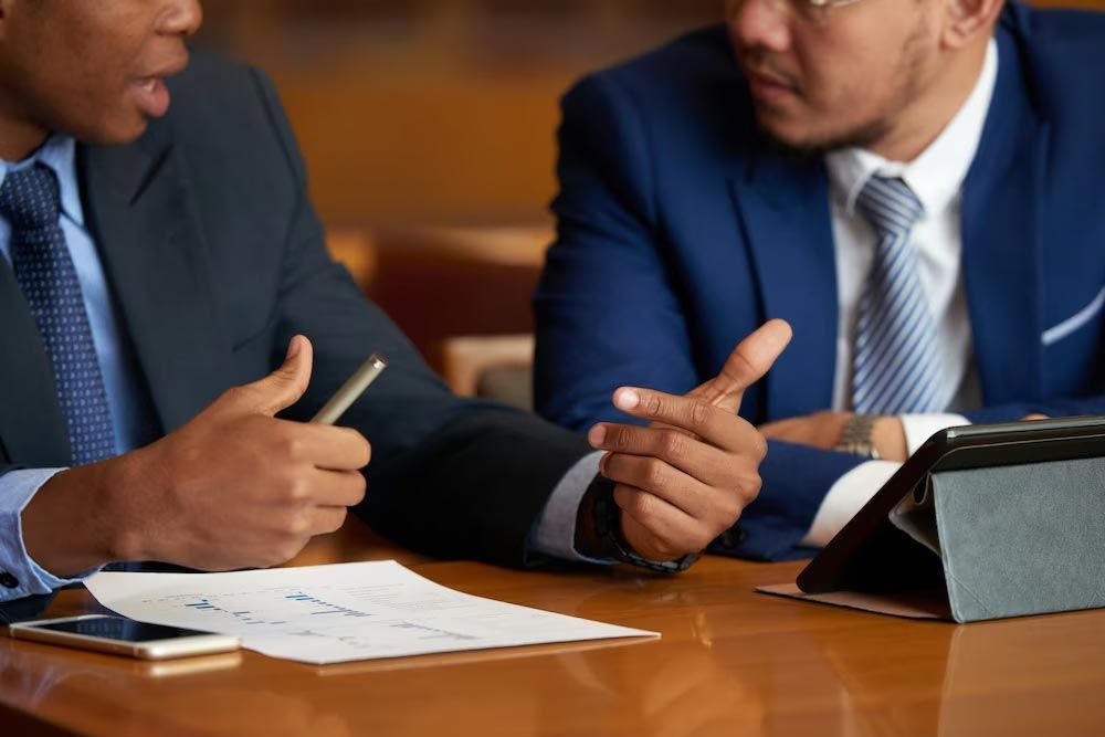 Two people in suits discussing documents at a conference table with a tablet nearby