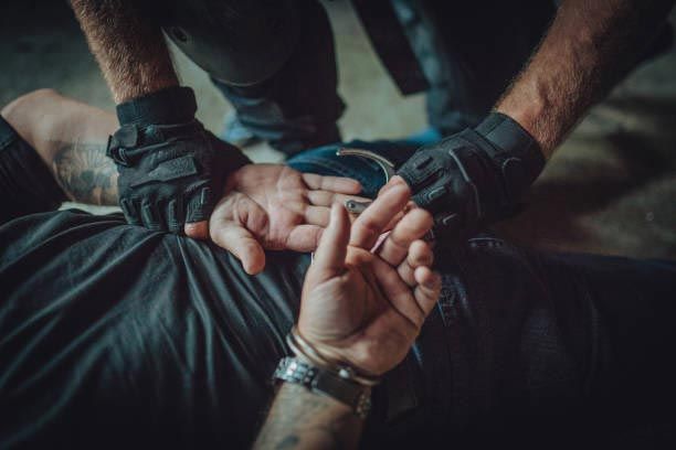 Handcuffed person lying down while two gloved hands restrain their wrists