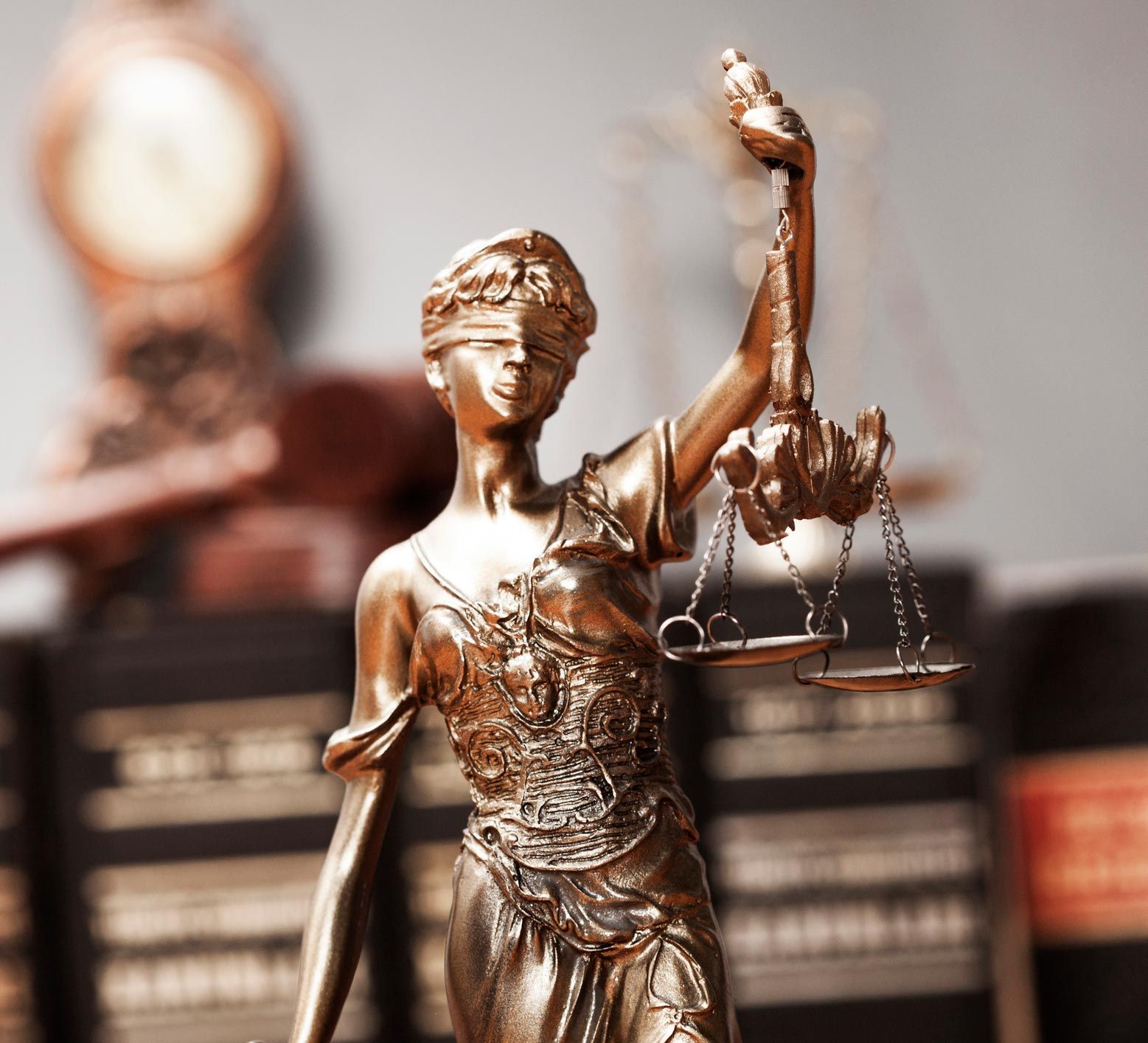 Bronze Lady Justice statue holding scales, with books blurred in the background