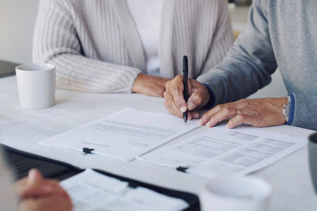 Two people signing paperwork at a table with open documents and coffee cups