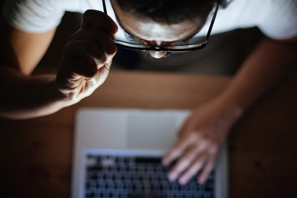 Person leaning over a laptop, typing in a dimly lit room