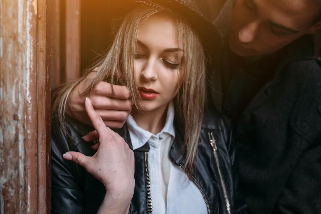 Two people standing close together by a wooden wall, one woman with eyes closed in warm, moody light