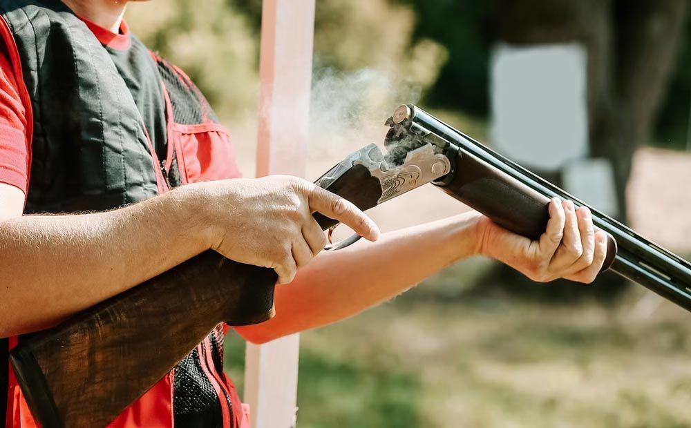 Person holding a shotgun outdoors, aiming it at a clay target in a shooting range