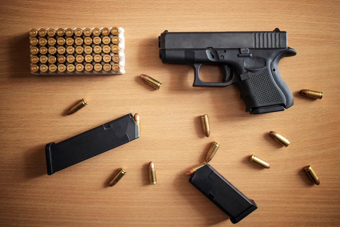 Handgun, two magazines, and loose bullets arranged on a wooden table