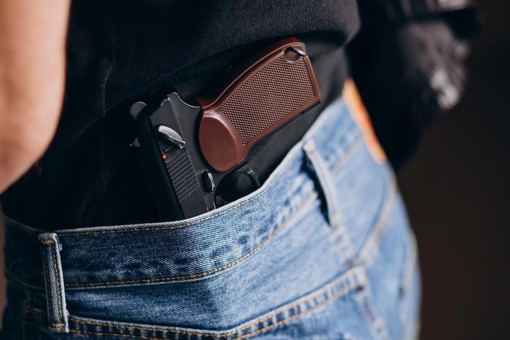 Handgun tucked into the back pocket of blue jeans against a black shirt