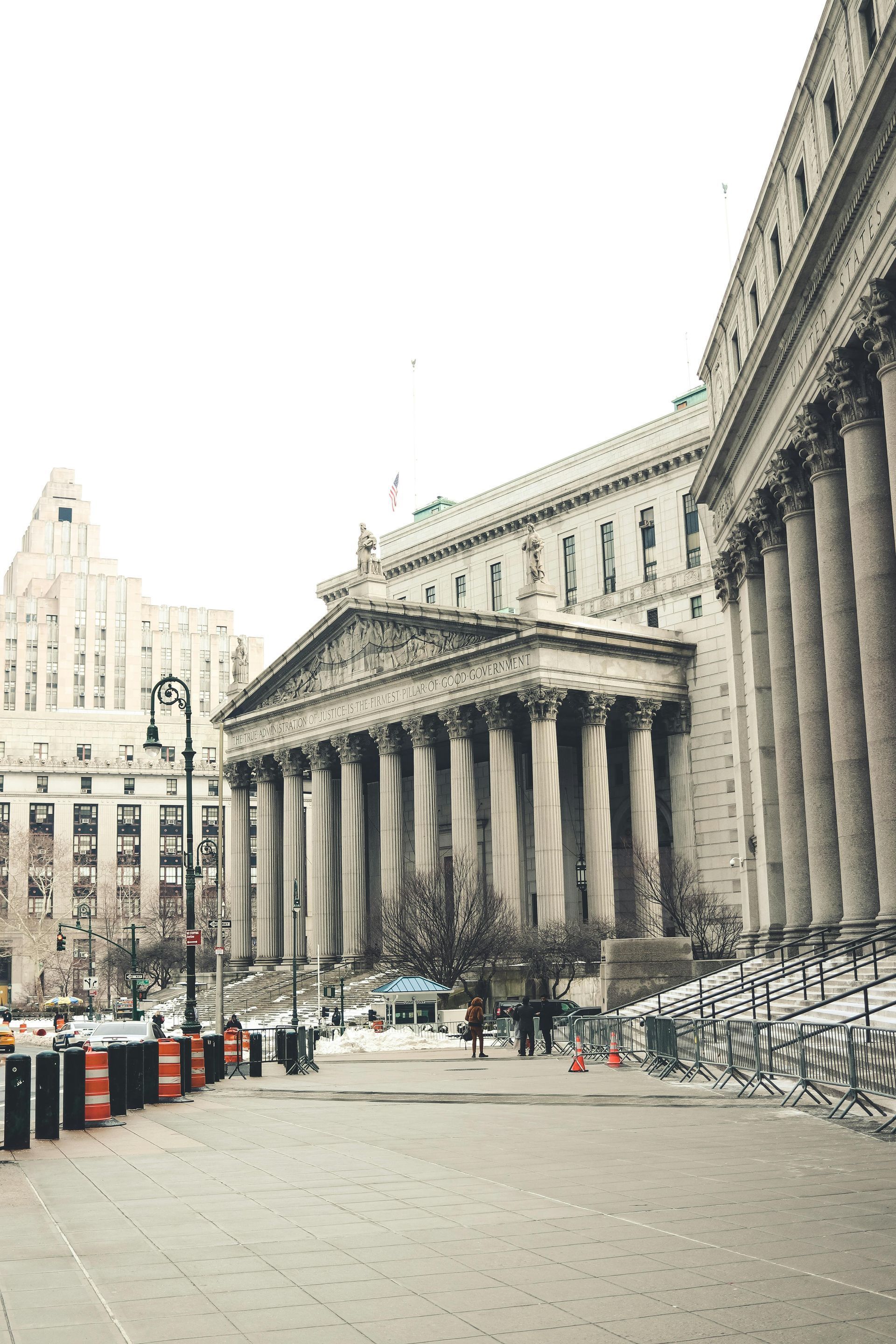 Grand neoclassical building with columns beside an open plaza and street, under an overcast sky