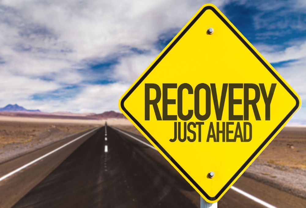 A sign on a desert highway that says 'Recovery Just Ahead'