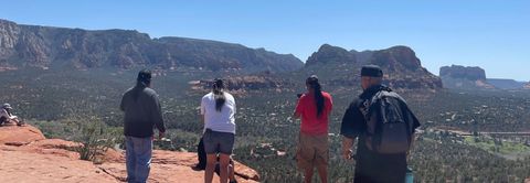 A group of people are standing on top of a hill looking at the mountains.