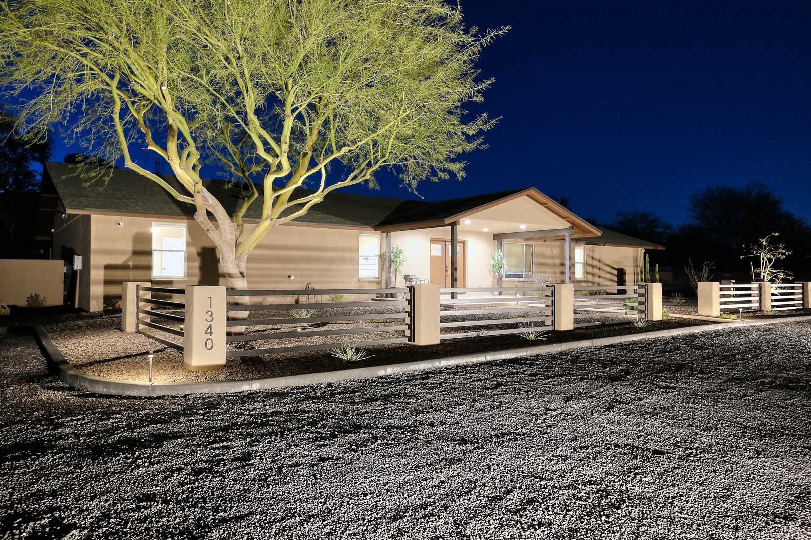 A house with a fence and a tree in front of it at night.
