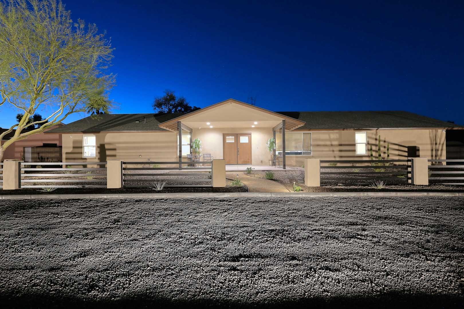 A house with a fence and a tree in front of it at night