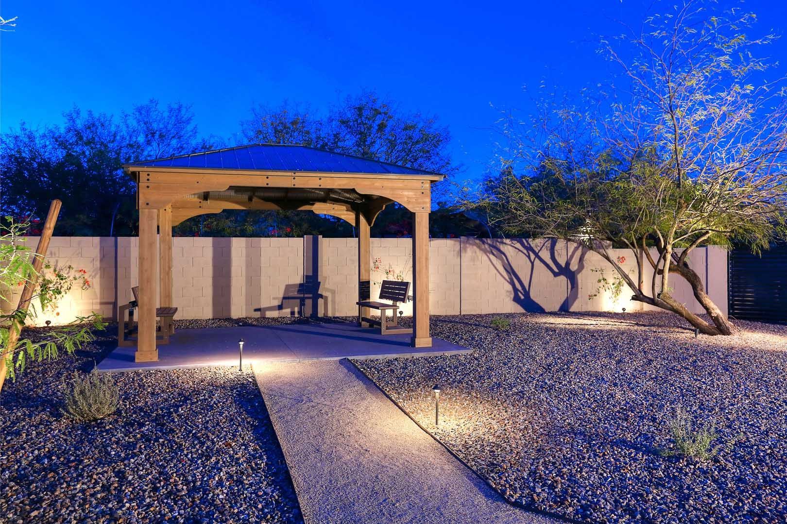 A gazebo is lit up at night in a backyard.