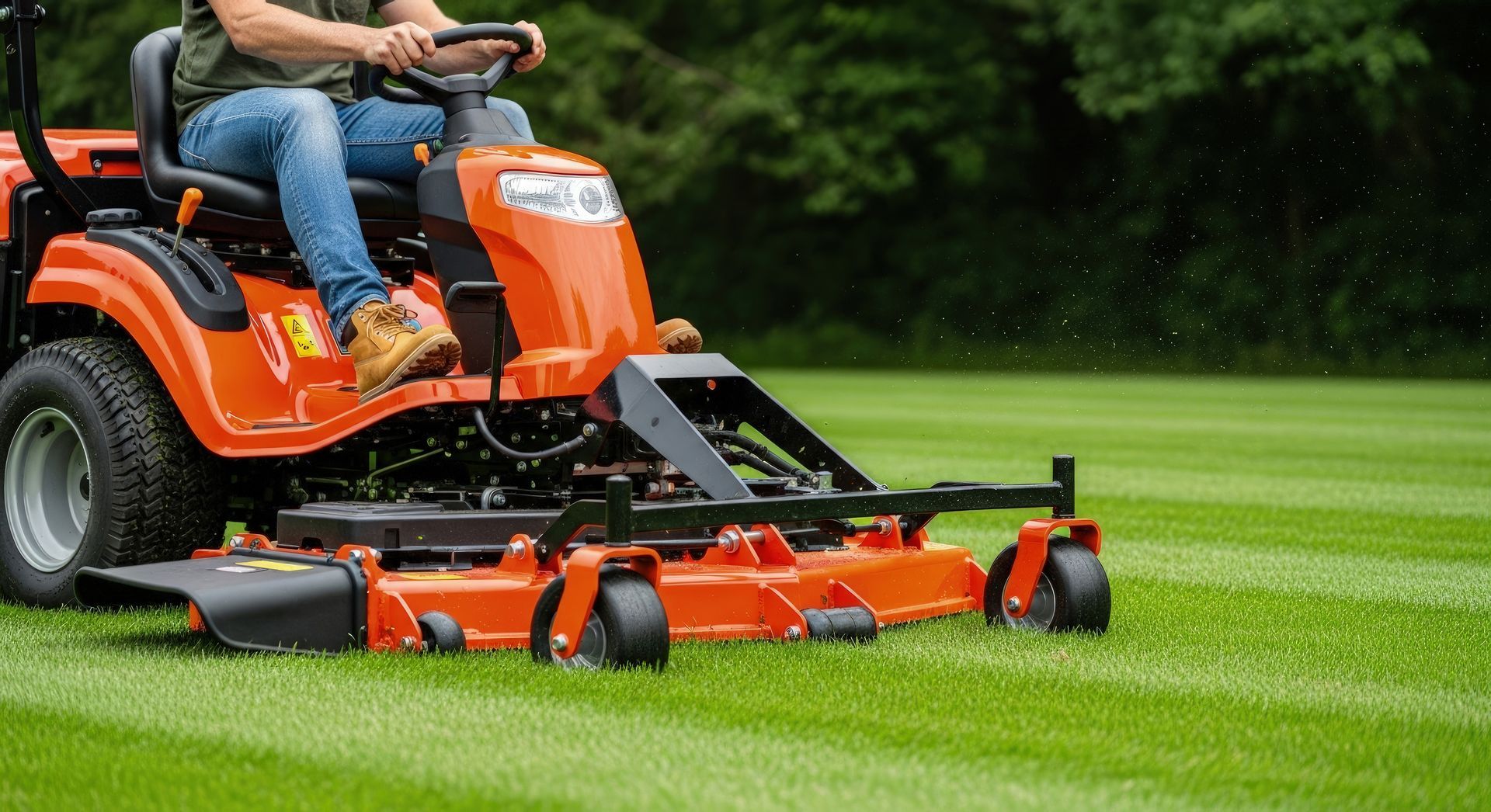 A man operating an orange riding lawn mower is cutting green grass on a large lawn near trees A man operating an orange riding lawn mower is cutting green grass on a large lawn near trees