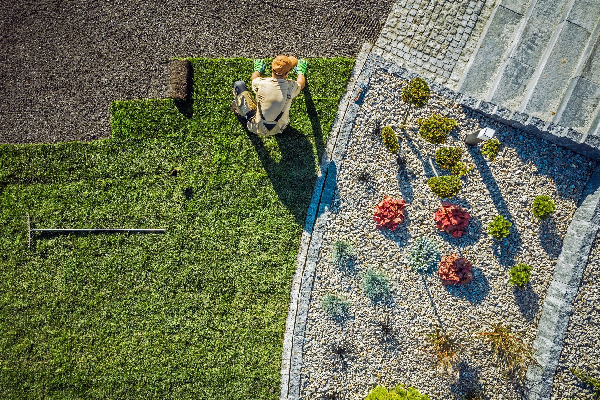 A worker is manually laying sod rolls onto prepared soil.