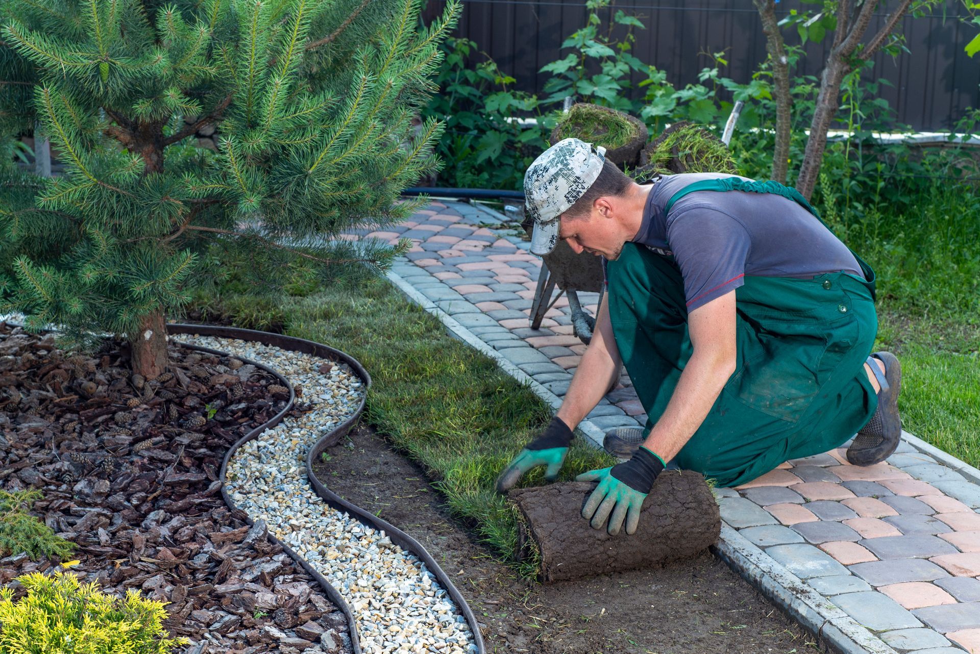 A worker is laying sod along a garden path with a decorative edging.