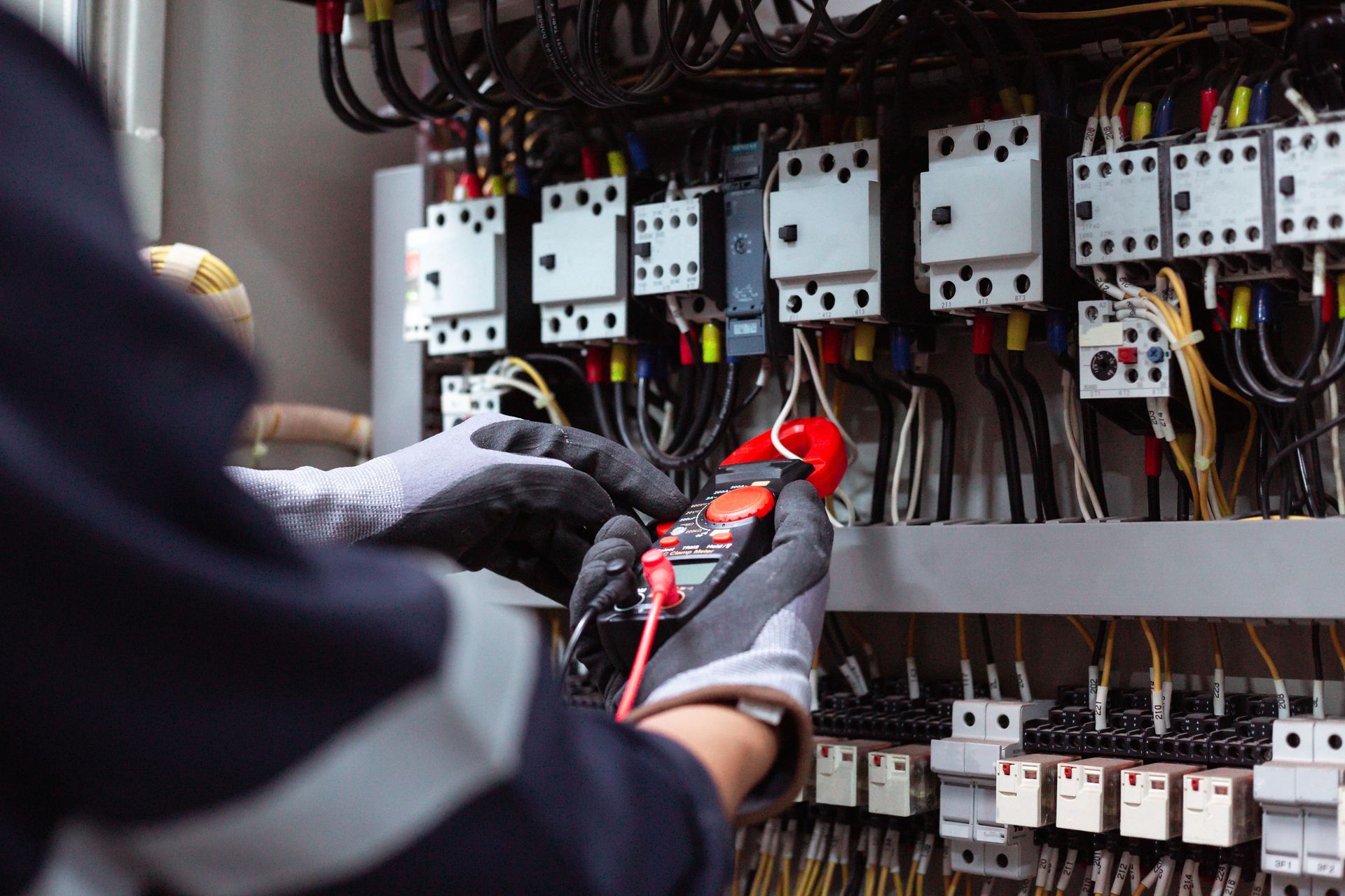 Electrician testing circuits inside an electrical control panel with a multimeter
