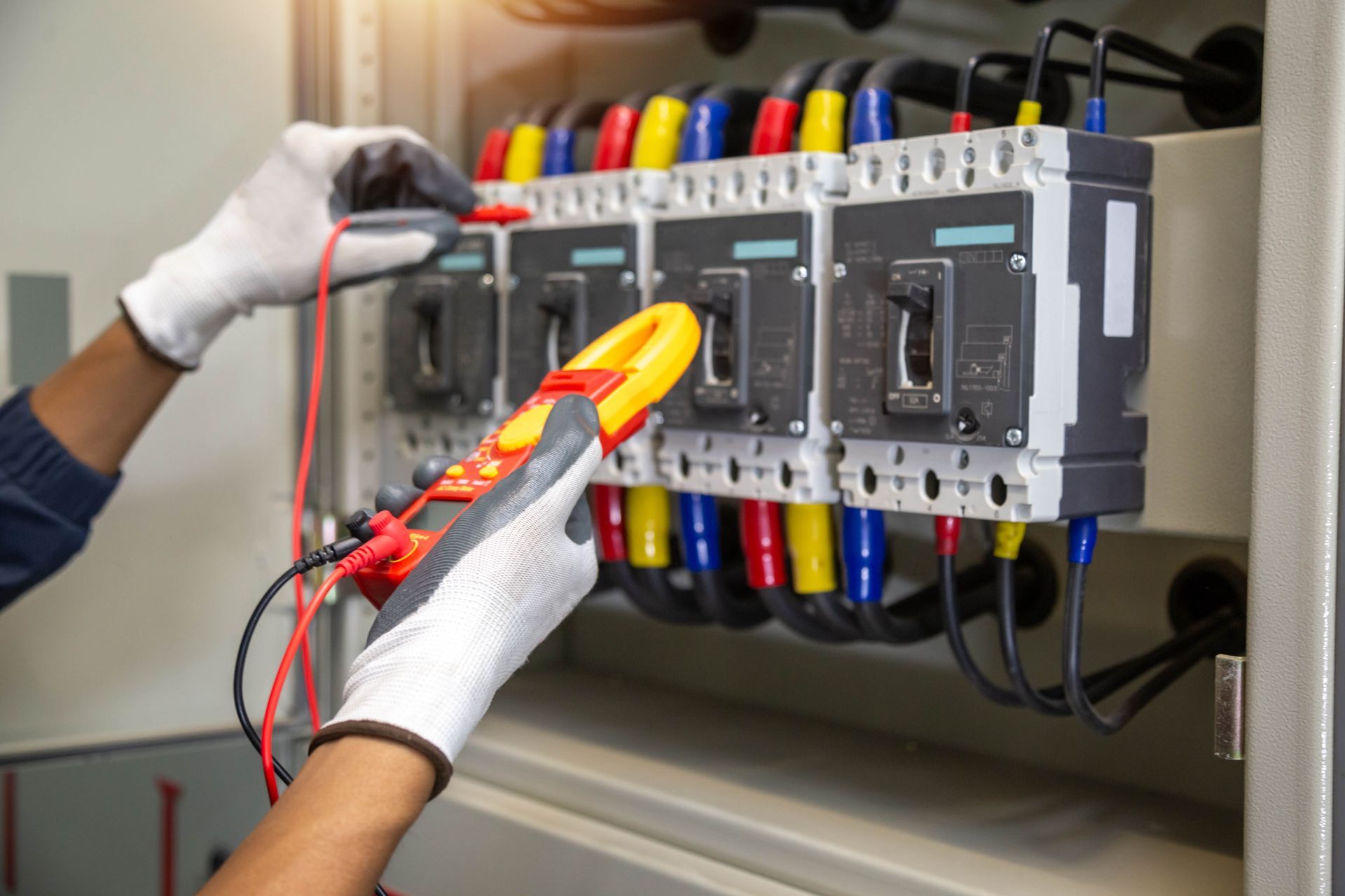 Technician testing electrical breakers inside a control panel with a clamp meter