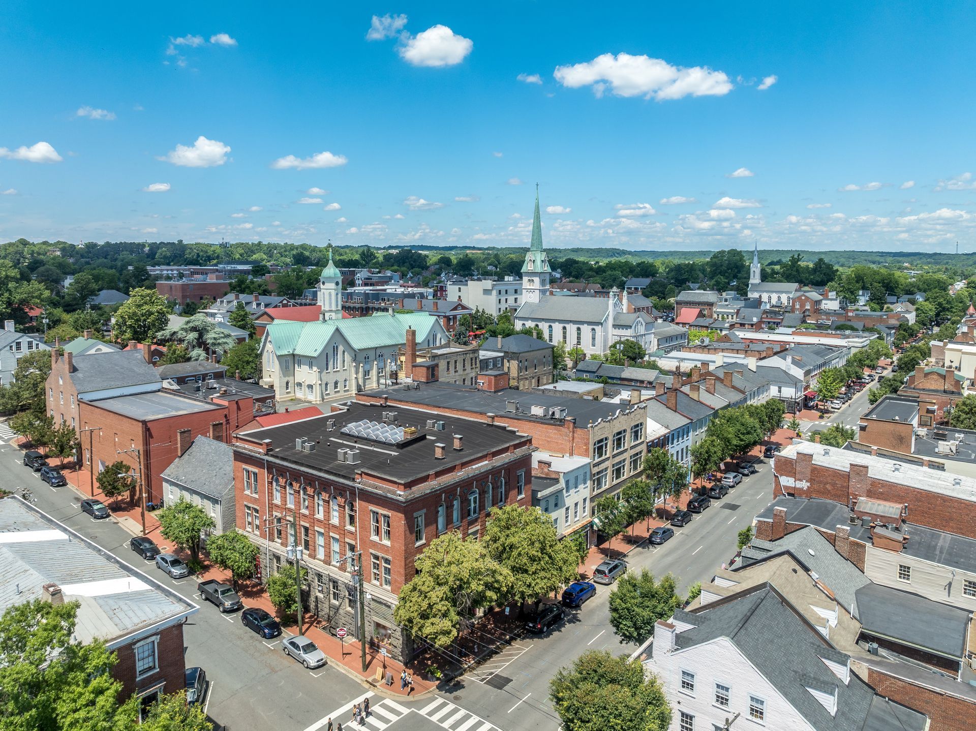 Aerial view of a small downtown with brick buildings, church steeples, and streets under a blue sky with clouds
