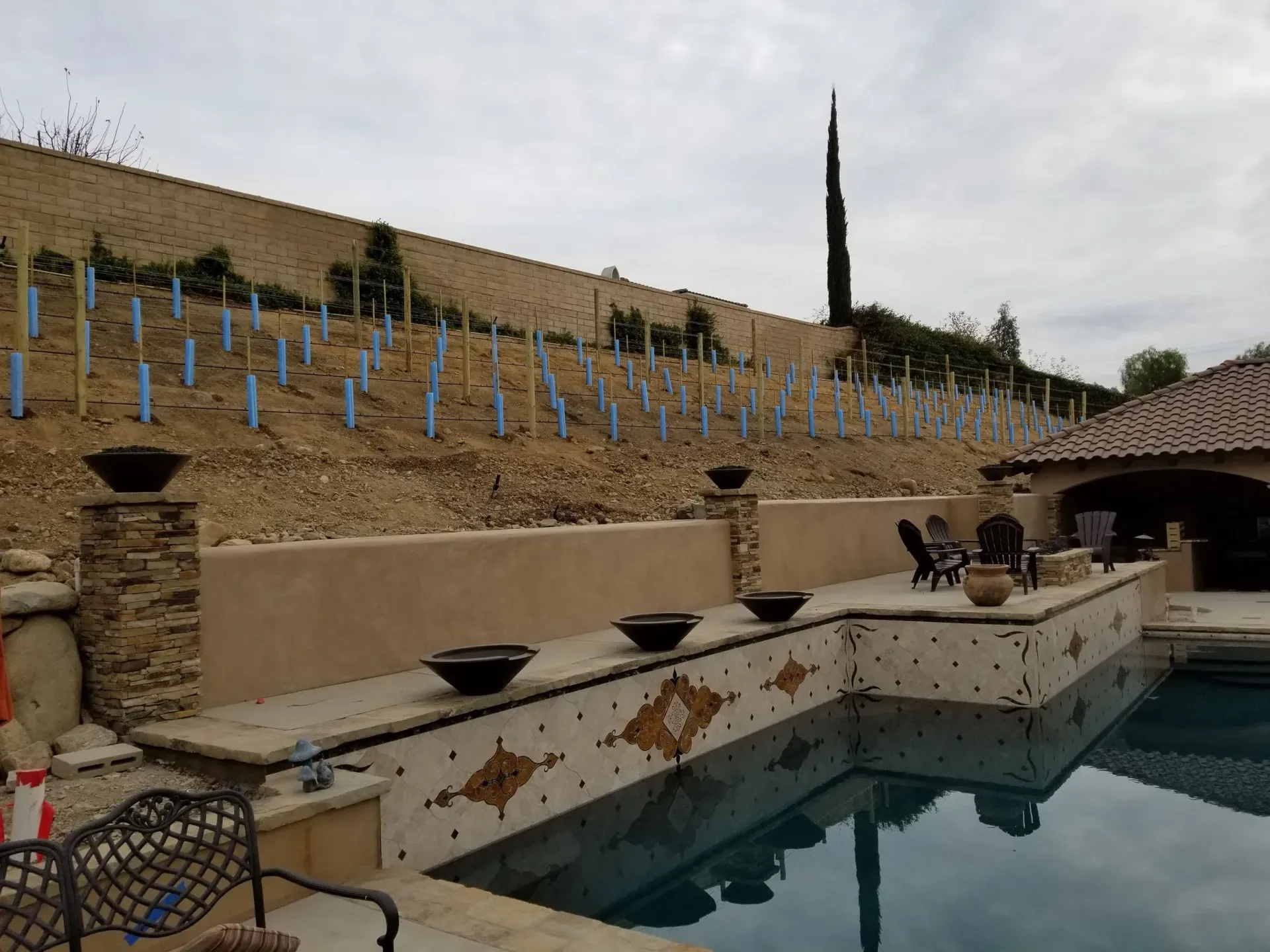 Poolside view with vineyard hillside, retaining wall, and water feature.