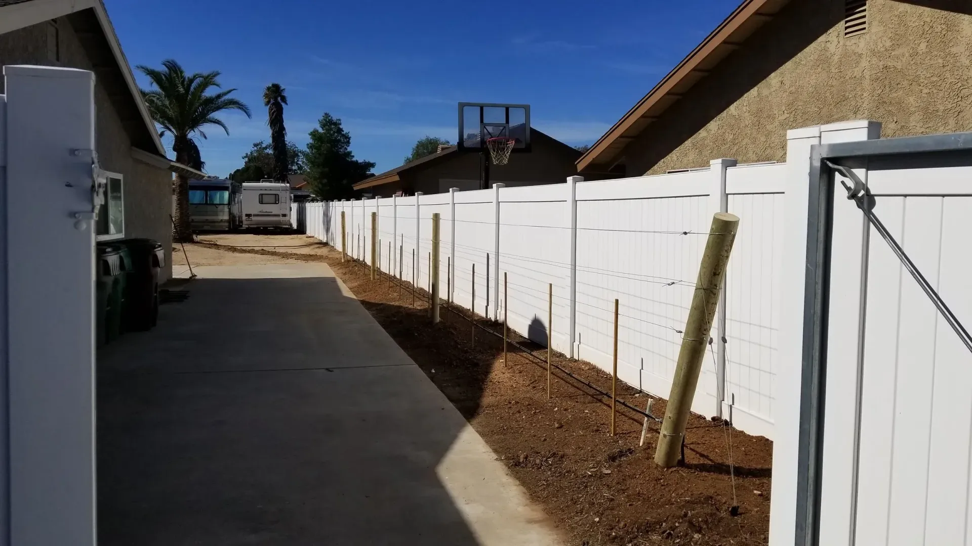 White fence borders a concrete alleyway with a basketball hoop visible.