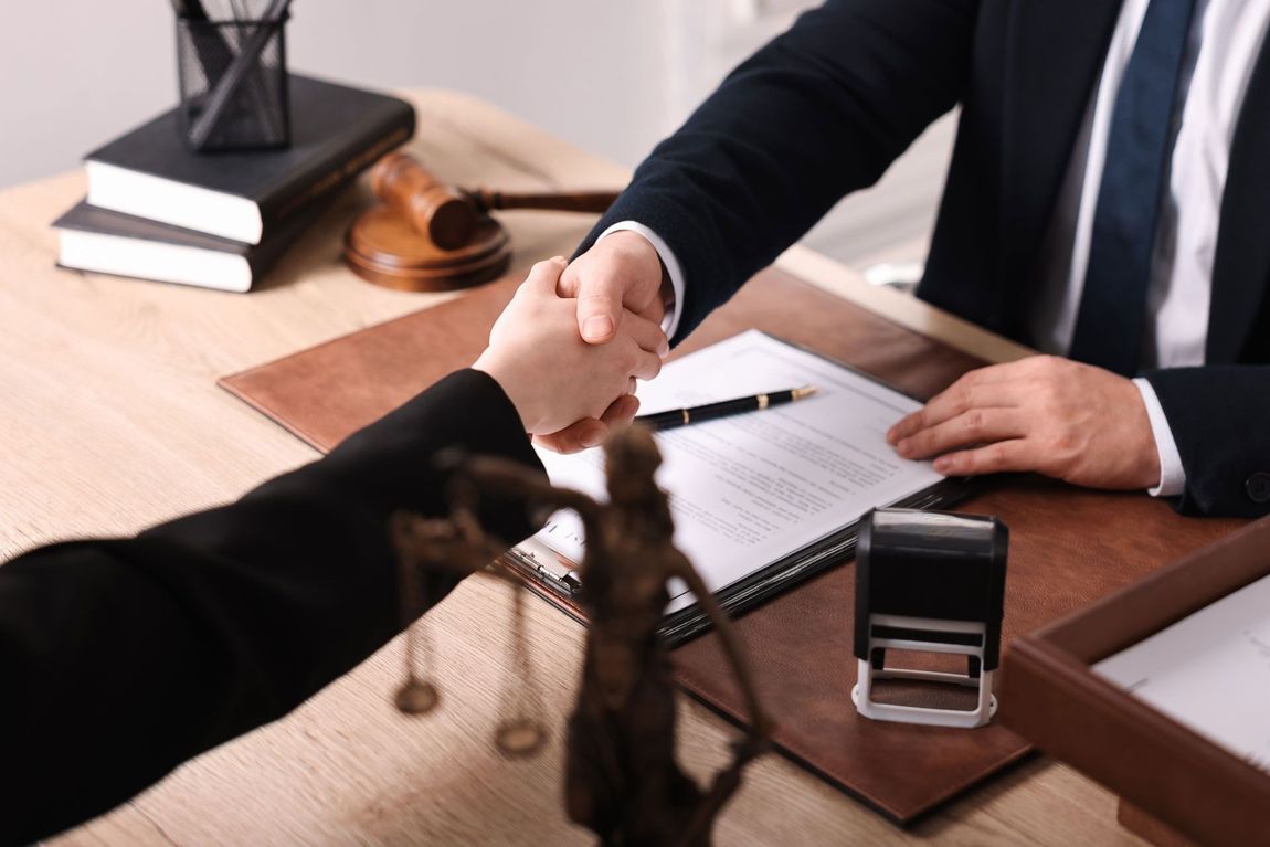A lawyer is shaking hands with a client while sitting at a desk