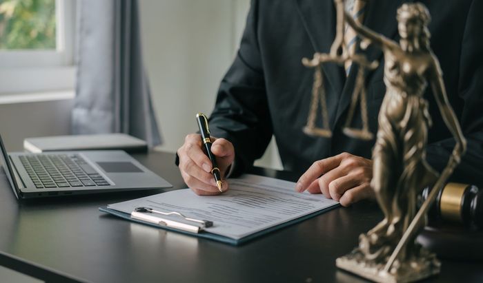 A lawyer is sitting at a desk with a statue of justice and a laptop