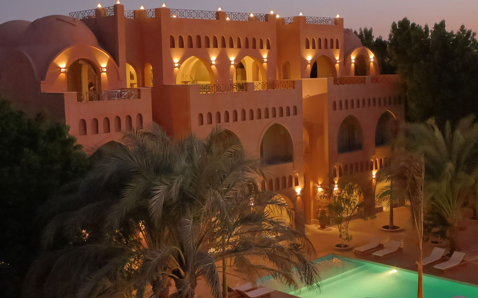 Lit orange villa with arches and palm trees at dusk beside a lit pool