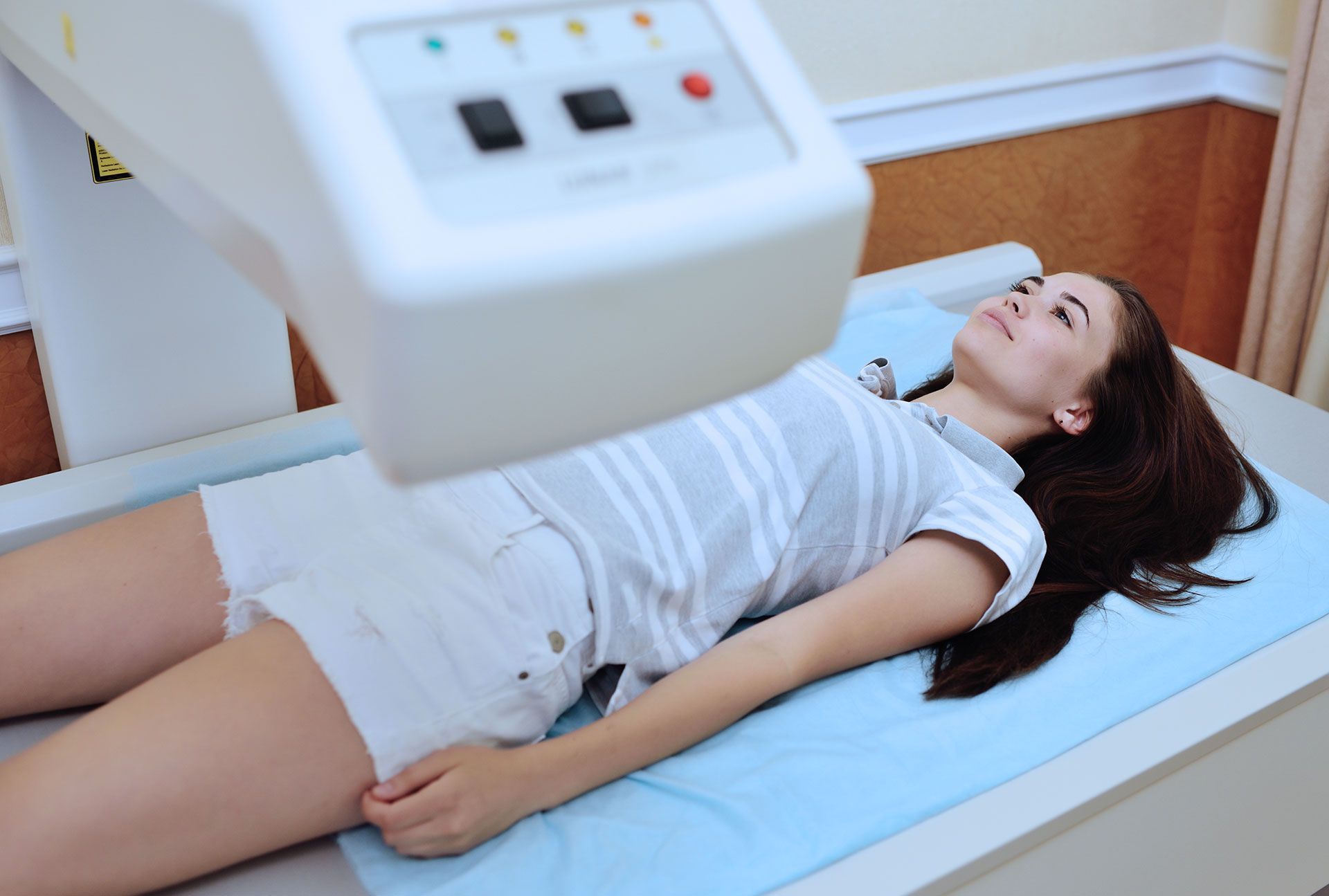 Woman undergoing a bone density scan, lying on a table in a medical setting.
