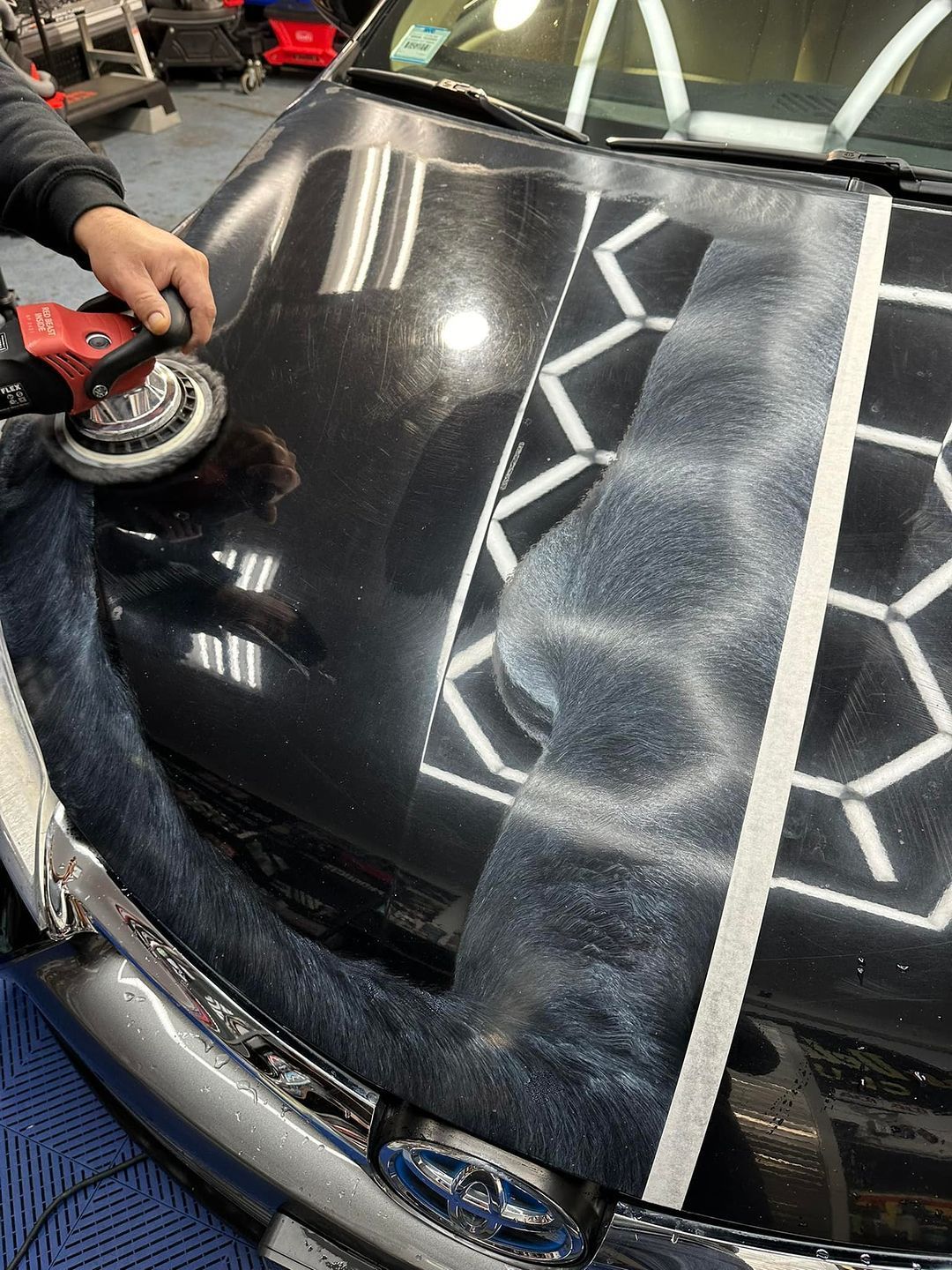 A person is polishing the hood of a black car.