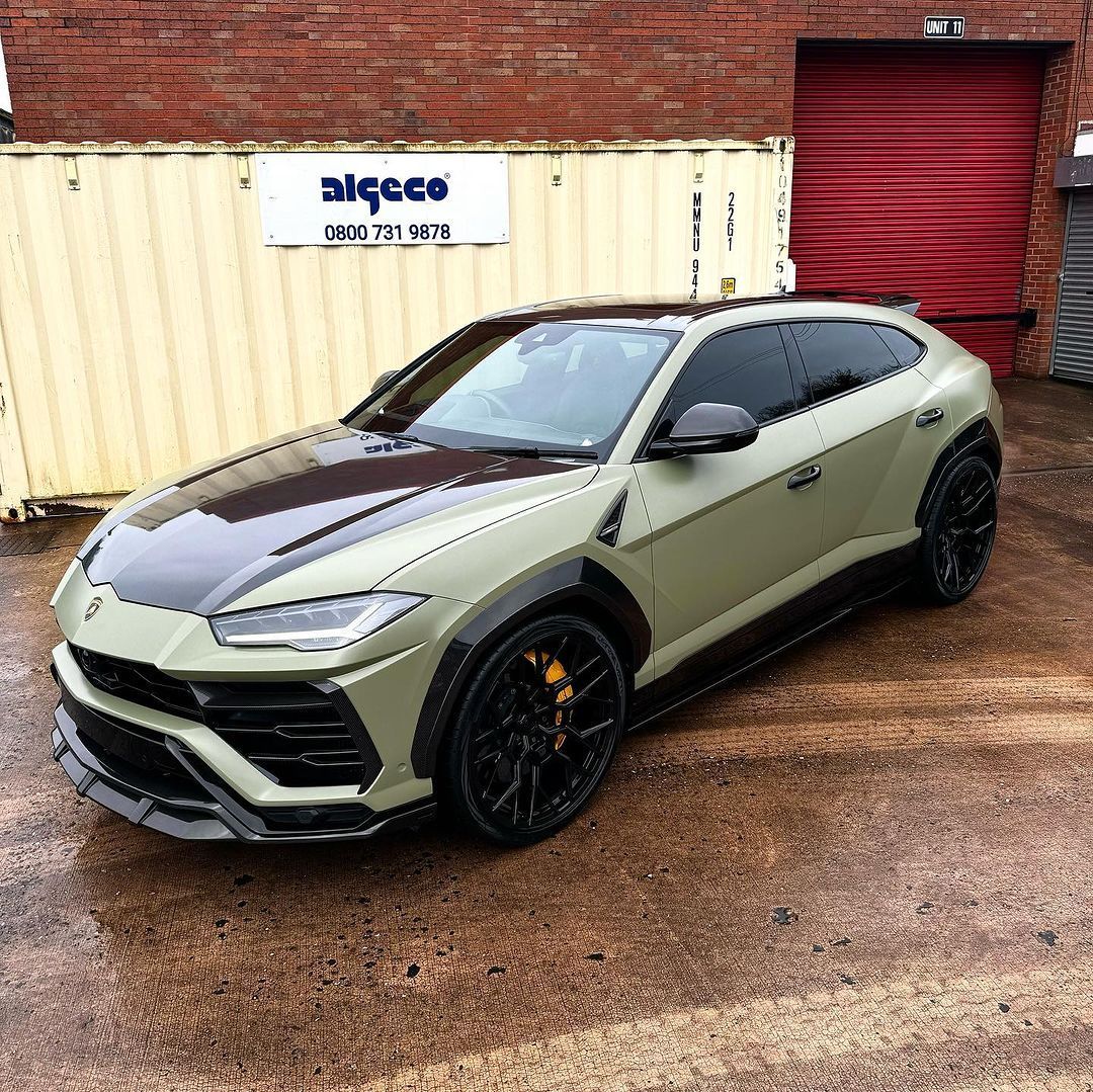 A green lamborghini urus is parked in front of a brick building.