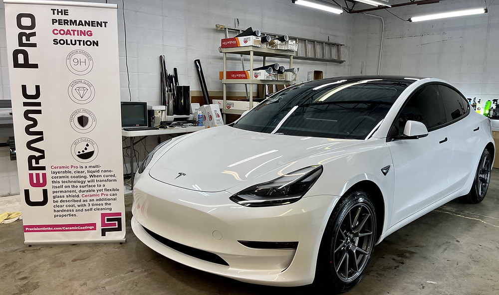 A white tesla model 3 is parked in a garage next to a ceramic pro sign.