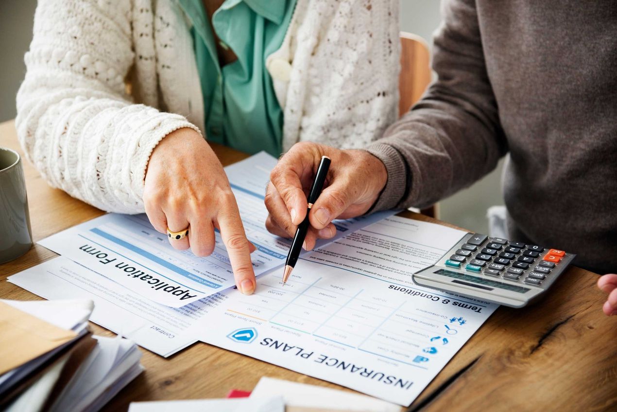 Hands pointing at insurance plan forms with a calculator on a wooden table.