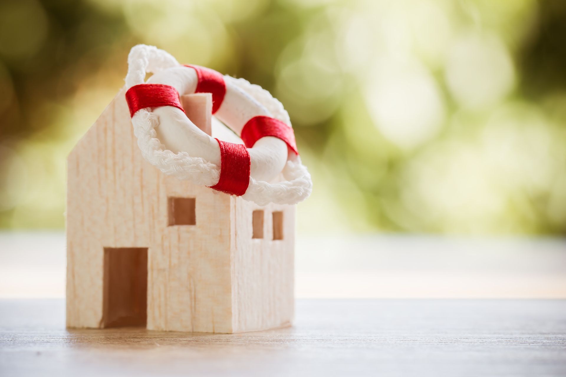 Wooden house model wrapped with a life preserver ring symbolizing insurance protection.
