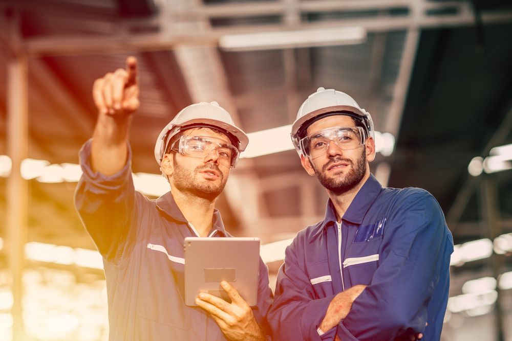 Two men are standing next to each other in a factory looking at a tablet.