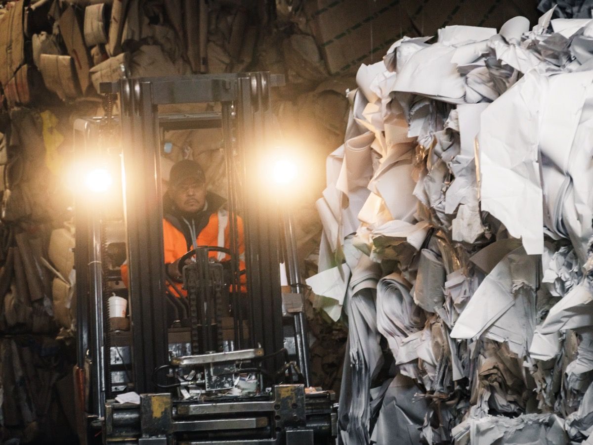 A Man Is Driving a Forklift in Front of A Pile of Paper. A Man Is Driving a Forklift in Front of A Pile of Paper.