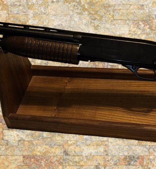 Black shotgun resting in a wooden display box on a patterned stone surface