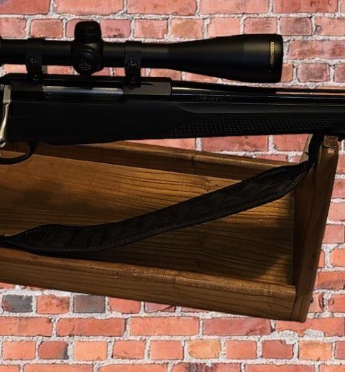 Black rifle with scope resting on a wooden stock against a brick wall background
