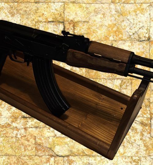 Black rifle resting on a wooden stand against a stone-pattern background.