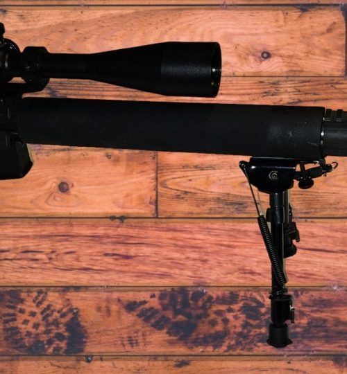 Black rifle mounted on a bipod against a wooden plank background.