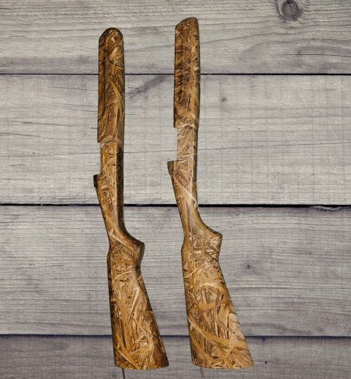 Two carved wooden gun stocks standing upright on a gray wood plank background