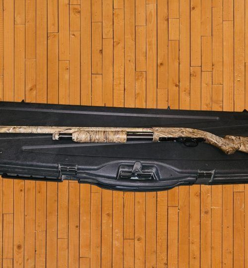 A long gun in a black case on a wooden floor, with a camouflaged stock and barrel.