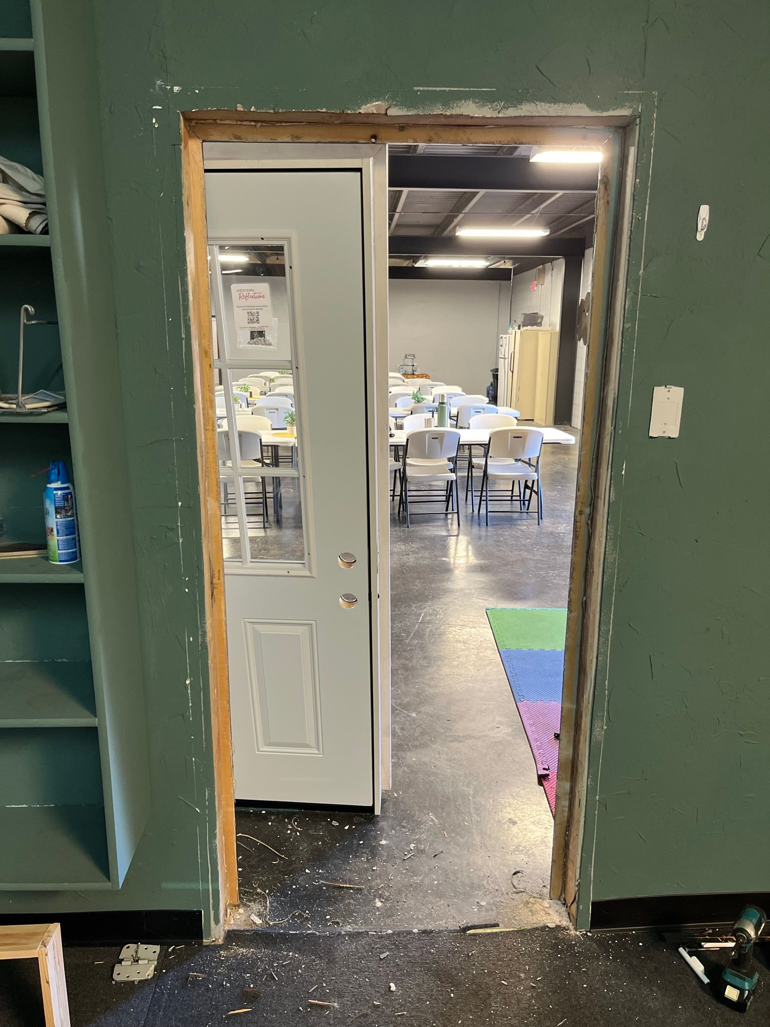 A doorway with a white door open to a room with tables and chairs; the doorway is under construction.