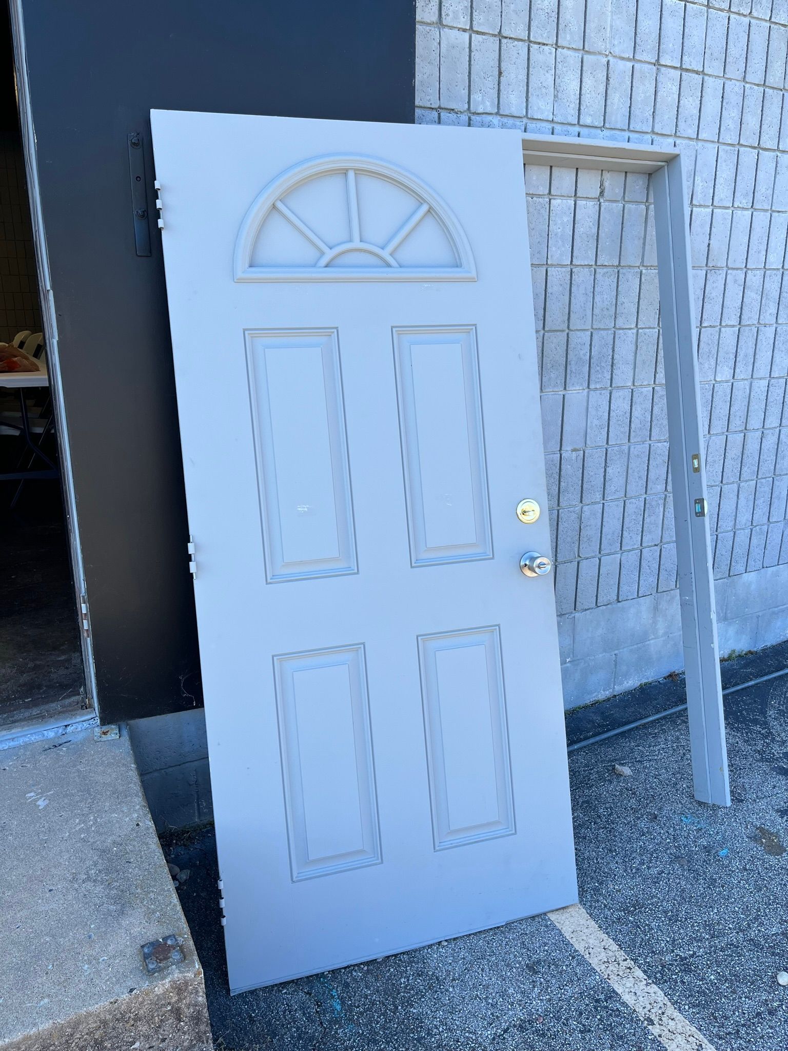 Gray door with an arched top, leaning against a gray brick wall with the door frame.